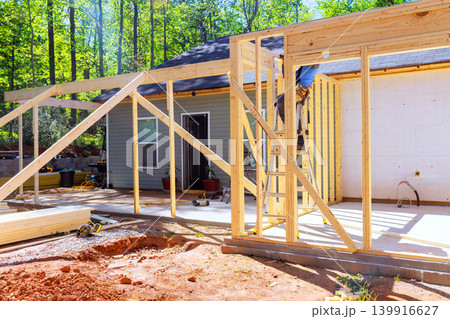 Workers install wooden beams for home extension in wooded area during trusses frame Workers install wooden beams for home extension in wooded area during trusses frame 139916627