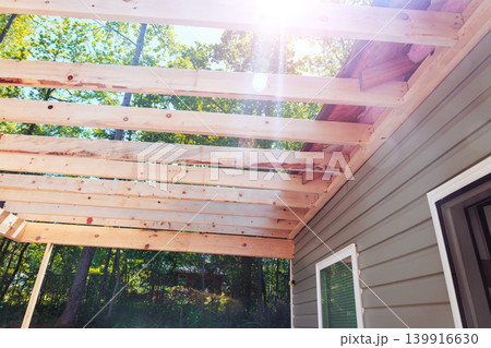 Wooden beams are being installed for pergola next to house in forested area during frameworks 139916630