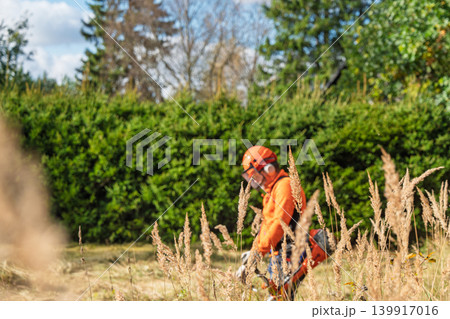 Brush cutter operator in protective gear trimming grass in Czech Republic countryside Brush cutter operator in protective gear trimming grass in Czech Republic countryside 139917016