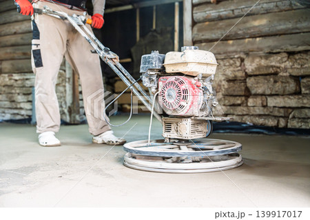 Construction worker using a power trowel to smooth and finish a concrete floor surface during a Construction worker using a power trowel to smooth and finish a concrete floor surface during a 139917017
