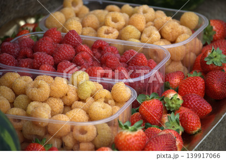 Display of fresh berries including strawberries, red and golden raspberries in plastic containers 139917066