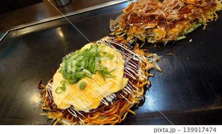 鉄板の上で焼かれる美味しそうな広島風お好み焼きとモダン焼き 139917474