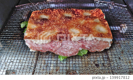 網の上で香ばしく焼かれた具だくさんのサラミフォカッチャサンド 139917812