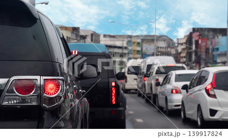 Tight rear view of black vehicle stopped on the asphalt road. City traffic during the day. Long queue of diverse many cars stretches ahead down a congested urban lane. Traffic congestion in Thailand. Tight rear view of black vehicle stopped on the asphalt road. City traffic during the day. Long queue of diverse many cars stretches ahead down a congested urban lane. Traffic congestion in Thailand. 139917824
