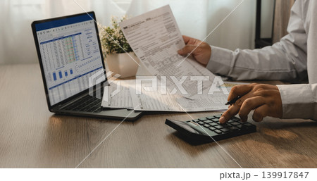 Accountant reviewing financial report and tax documents on laptop while using calculator for account analysis, real estate investment planning, expense management, and reporting workflow. Accountant reviewing financial report and tax documents on laptop while using calculator for account analysis, real estate investment planning, expense management, and reporting workflow. 139917847