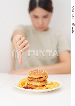 woman showing thumbs down, Rejecting and refusing with Juicy beef burger, potato chips and carbonated Soft drinks. Unhealthy, High calorie, Fast food craving, Obesity, diet, weight loss and junk food 139919278