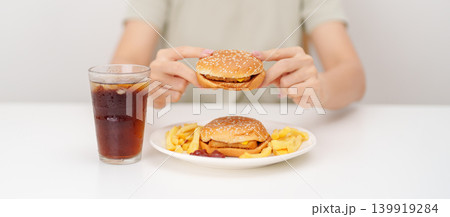 woman eating Juicy beef burger with melted cheddar cheese, potato chips and carbonated Soft drinks. Unhealthy, High calorie, Fast food craving, Obesity, diet, weight loss, junk food and lifestyle woman eating Juicy beef burger with melted cheddar cheese, potato chips and carbonated Soft drinks. Unhealthy, High calorie, Fast food craving, Obesity, diet, weight loss, junk food and lifestyle 139919284