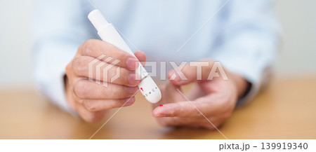 Hand using lancet pen on finger with Blood drop glucose testing or Diabetes checking by digital blood glucose meter. blood sugar level, Diabetes Day, Glycemia, Hypoglycemia, Hyperglycemia and insulin 139919340