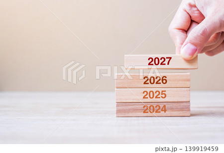 2027 block over 2026 and 2025 wooden building on table background. Business planning, Risk Management, Resolution, strategy, solution, goal, New Year New You and happy holiday concepts 139919459