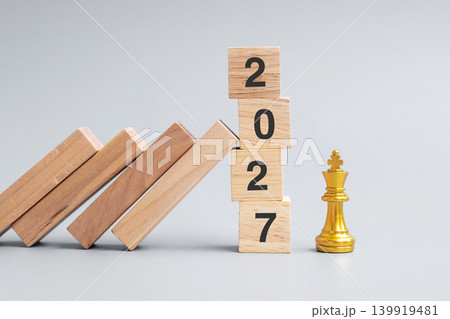 wooden Dominoes falling against 2027 stop blocks with golden Chess King figure. Business, Risk Management, Solution, economic, Insurance and New Year concept 139919481