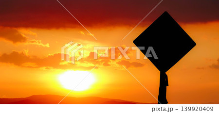 西の空に沈む夕陽の光でシルエットになった道路標識のある風景 139920409