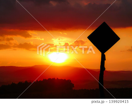 西の空に沈む夕陽の光でシルエットになった道路標識のある風景 西の空に沈む夕陽の光でシルエットになった道路標識のある風景 139920415