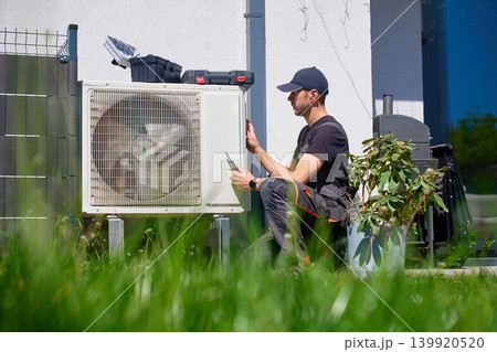 HVAC technician servicing outdoor unit near house 139920520