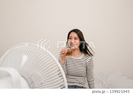 家の中で扇風機の風にあたりながら麦茶を飲む笑顔の女性 家の中で扇風機の風にあたりながら麦茶を飲む笑顔の女性 139921045