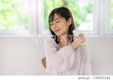 マッサージガンで肩をセルフマッサージする日本人の若い女性 マッサージガンで肩をセルフマッサージする日本人の若い女性 139923548