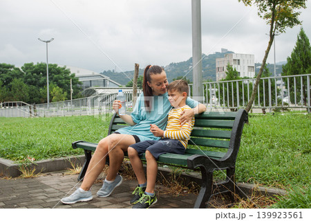 Brunette mother and her young son relaxing outdoors. Tired child with mom Brunette mother and her young son relaxing outdoors. Tired child with mom 139923561