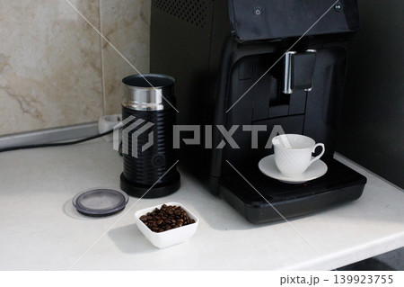 In a kitchen, a coffee machine is on the countertop. Coffee beans are next to the machine. In a kitchen, a coffee machine is on the countertop. Coffee beans are next to the machine. 139923755