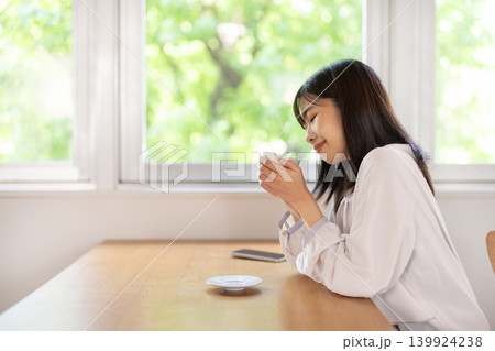 窓際のテーブルでコーヒーを楽しむ日本人の若い女性 139924238