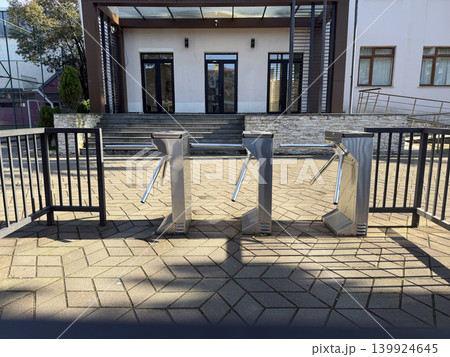Turnstiles stand in front of a building with stairs and a fence at a public location during daytime 139924645