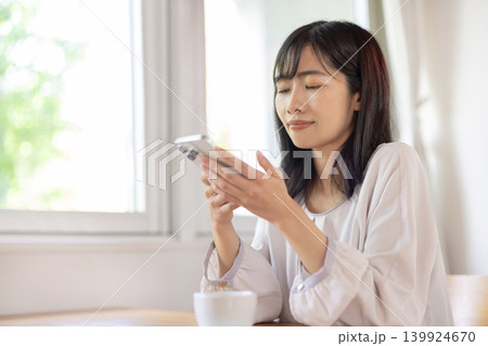 窓際のテーブルでスマートフォンを操作する日本人の若い女性 139924670