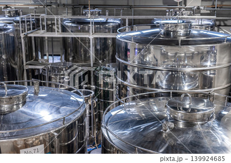 Large shiny stainless steel storage tanks inside modern industrial factory facility displaying complex piping systems used for commercial liquid beverage production process Large shiny stainless steel storage tanks inside modern industrial factory facility displaying complex piping systems used for commercial liquid beverage production process 139924685