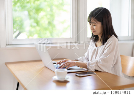 明るい窓際のテーブルでパソコン作業をする日本人の若い女性 明るい窓際のテーブルでパソコン作業をする日本人の若い女性 139924911