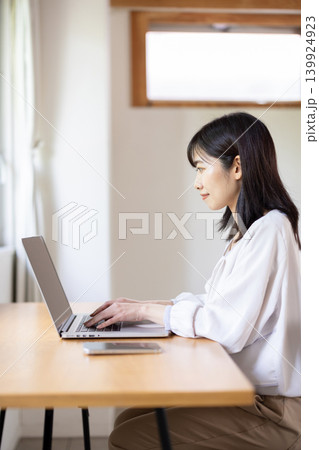 明るい窓際のテーブルでパソコン作業をする日本人の若い女性 139924923