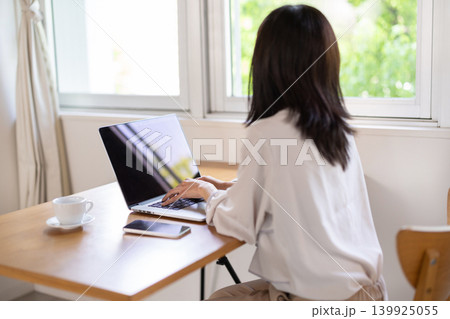 窓際のテーブルでパソコン作業をする女性の後ろ姿 139925055