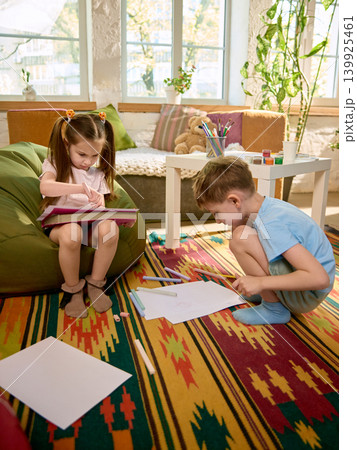 Children drawing with chalk and pastels on colorful rug in sunny creative room Children drawing with chalk and pastels on colorful rug in sunny creative room 139925461