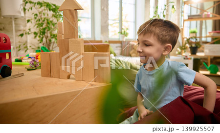 Boy building wooden block tower in cozy playroom with soft natural light. Boy building wooden block tower in cozy playroom with soft natural light. 139925507