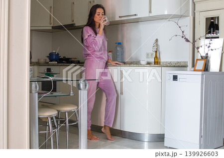 Brunette mature woman drinking a glass of water in a modern kitchen. Healthy lifestyle Brunette mature woman drinking a glass of water in a modern kitchen. Healthy lifestyle 139926603