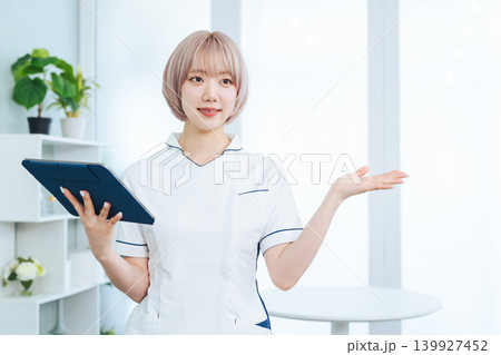 タブレットPCを持って案内するハイトーンヘアの女性スタッフ 139927452
