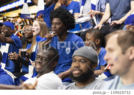 Black father with vuvuzela spending quality time with son at soccer stadium full of cheering fans. Football lifestyle, parenthood and family bonding, blue team support and childhood joy. 139928732