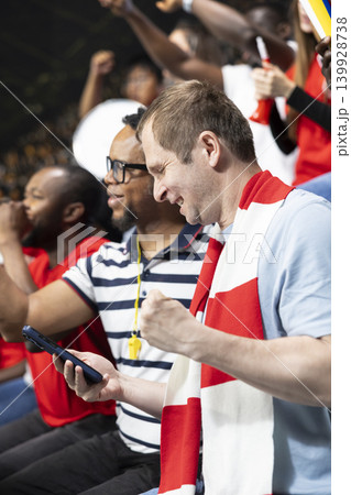 Diverse football fans cheering after winning live betting wager during soccer match surrounded by passionate stadium crowd. Supporters check betting apps and celebrating lucky win, jackpot feeling. Diverse football fans cheering after winning live betting wager during soccer match surrounded by passionate stadium crowd. Supporters check betting apps and celebrating lucky win, jackpot feeling. 139928738