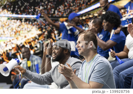 Blue soccer supporters cheering together in crowded stadium during live football match in the supporter section. Passionate sports fans celebrate together, crowd cheering and nonstop fan chants. 139928756