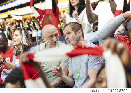 Excited sports fans checking online betting odds and cash out options on smartphone, live football match in the stadium stands. Passionate supporters tracking risky wagers on betting apps. Excited sports fans checking online betting odds and cash out options on smartphone, live football match in the stadium stands. Passionate supporters tracking risky wagers on betting apps. 139928762