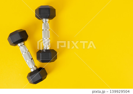Flat lay of Two black dumbbells lying on yellow background with copy space Flat lay of Two black dumbbells lying on yellow background with copy space 139929504