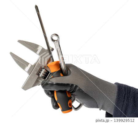 Gloved hand holding a group of tools like an adjustable wrench, screwdriver, and spanner isolated on white background Gloved hand holding a group of tools like an adjustable wrench, screwdriver, and spanner isolated on white background 139929512