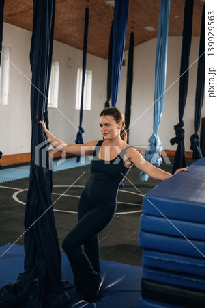 Pretty woman practicing aerial yoga on hammock straps in a fitness studio. Standing and smiling 139929563