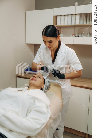 In black gloves. Female cosmetologist performing a facial skincare procedure using a cosmetic device in a beauty clinic In black gloves. Female cosmetologist performing a facial skincare procedure using a cosmetic device in a beauty clinic 139929815