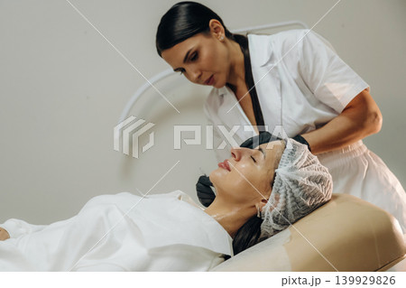 In black gloves. Female cosmetologist performing a facial skincare procedure using a cosmetic device in a beauty clinic In black gloves. Female cosmetologist performing a facial skincare procedure using a cosmetic device in a beauty clinic 139929826