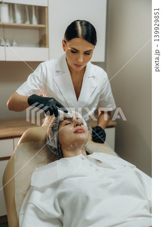 Dermatology conception. Female cosmetologist performing a facial skincare procedure using a cosmetic device in a beauty clinic 139929851