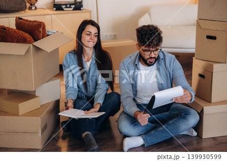 Sitting on the floor with notepads. Couple reviewing documents and planning their new home after moving Sitting on the floor with notepads. Couple reviewing documents and planning their new home after moving 139930599