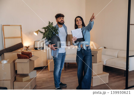 Man is with plant in hand. Couple reviewing documents and planning their new home after moving 139930621