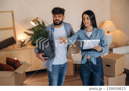 Man is with plant in hand. Couple reviewing documents and planning their new home after moving Man is with plant in hand. Couple reviewing documents and planning their new home after moving 139930623