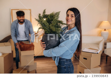 Looking at the camera and smiling. Positive couple placing a potted plant in their new apartment during the moving process 139930643