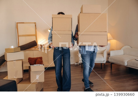 No faces visible, standing. A couple carrying cardboard boxes while moving into a new apartment No faces visible, standing. A couple carrying cardboard boxes while moving into a new apartment 139930660