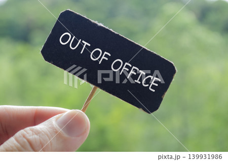 Hand holding a black out of office card against a soft blurred green background Hand holding a black out of office card against a soft blurred green background 139931986