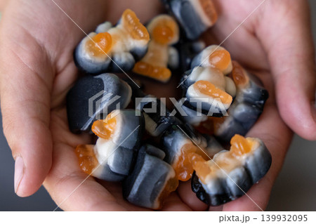 Close-up of hands holding colorful gummy candies in various shapes and colors, featuring orange and black hues, with a soft-focus background Close-up of hands holding colorful gummy candies in various shapes and colors, featuring orange and black hues, with a soft-focus background 139932095