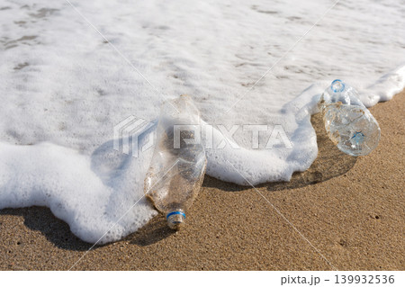 Sea foam washing over plastic bottles on a sandy shore. Water pollution, environmental hazard and ocean conservation concept. Sea foam washing over plastic bottles on a sandy shore. Water pollution, environmental hazard and ocean conservation concept. 139932536